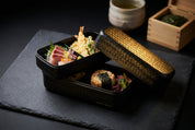 Boîte bento noire fermée avec couvercle à motif tressé.