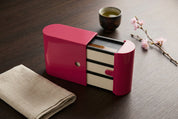 Boîtier bento rose ouvert laissant voir trois boîtes superposées.