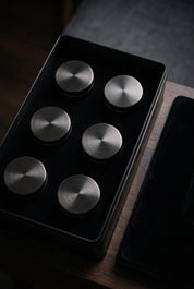 Coffret noir ouvert présentant six boîtes rondes dans leur rangement.
