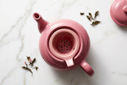 Vue de dessus de la théière rose et de son filtre en porcelaine perforé.